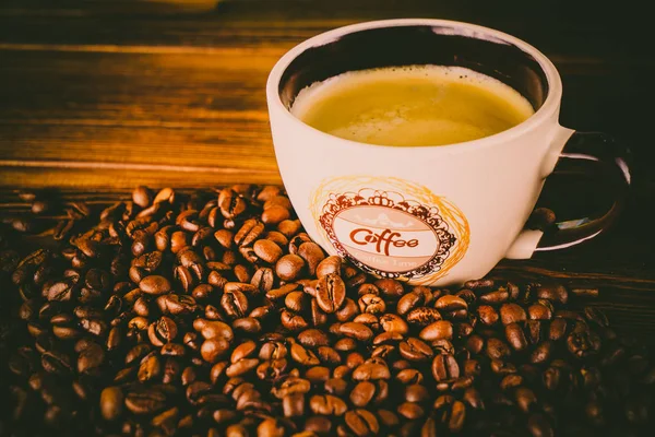 Tahta arka planda bir fincan kahve ve kahve çekirdeği.