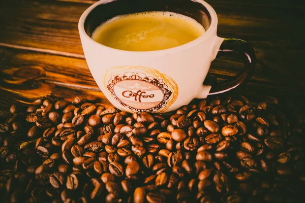 Tahta arka planda bir fincan kahve ve kahve çekirdeği.