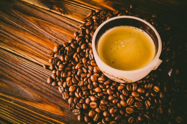 Tahta arka planda bir fincan kahve ve kahve çekirdeği.