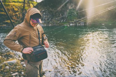 Balıkçı bir alabalık bir dağ nehir üzerinde yakalar.