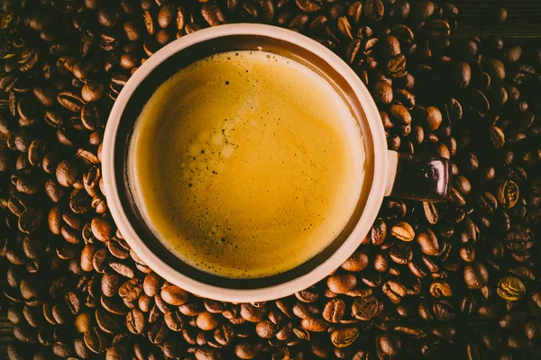 Tahta arka planda bir fincan kahve ve kahve çekirdeği.