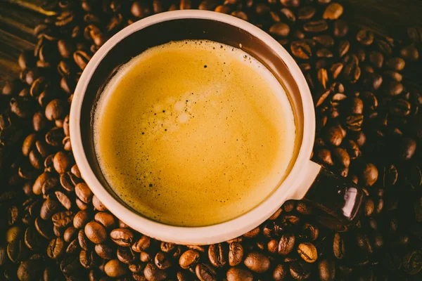 Tahta arka planda bir fincan kahve ve kahve çekirdeği.