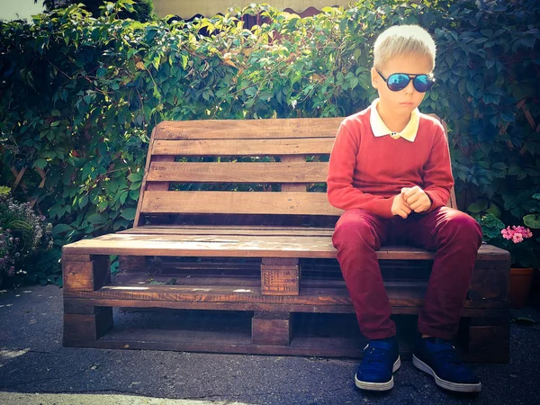 şık çocuk ahşap bir bankta oturur