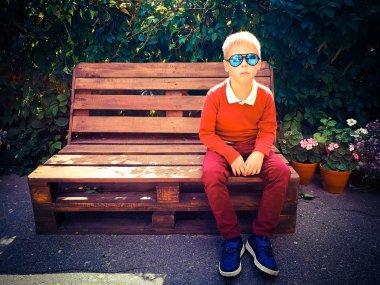 şık çocuk ahşap bir bankta oturur