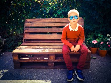 şık çocuk ahşap bir bankta oturur