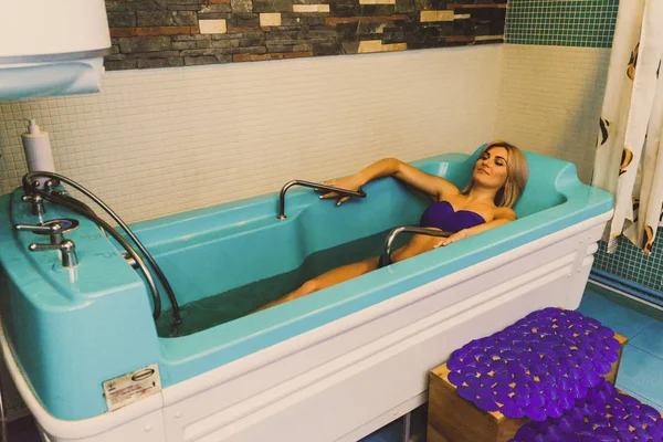 Blonde woman relaxing in spa salon, underwater massage.