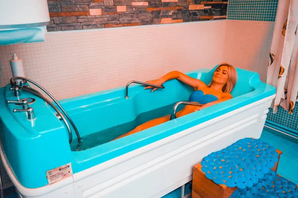 Blonde woman relaxing in spa salon, underwater massage.