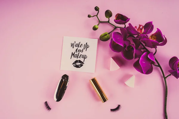 Інструменти для макіяжу на рожевому фоні та квітка орхідеї — стокове фото