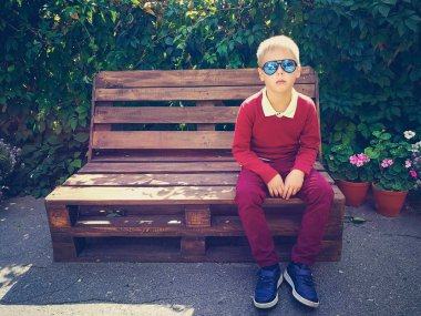 şık çocuk ahşap bir bankta oturur