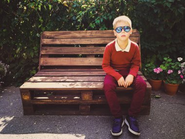 şık çocuk ahşap bir bankta oturur