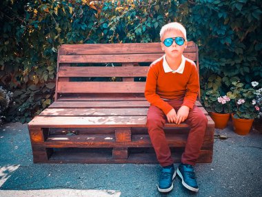 şık çocuk ahşap bir bankta oturur