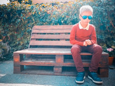 şık çocuk ahşap bir bankta oturur