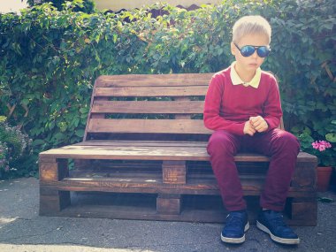 şık çocuk ahşap bir bankta oturur