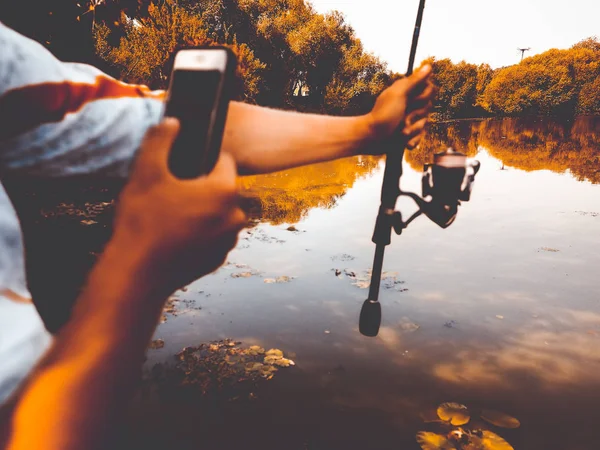 Rybář loví v létě na jezeře s telefonem — Stock fotografie