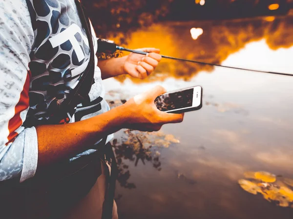 Rybář loví v létě na jezeře s telefonem — Stock fotografie