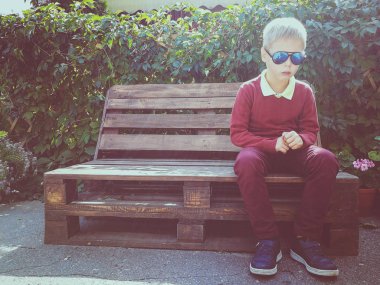 şık çocuk ahşap bir bankta oturur