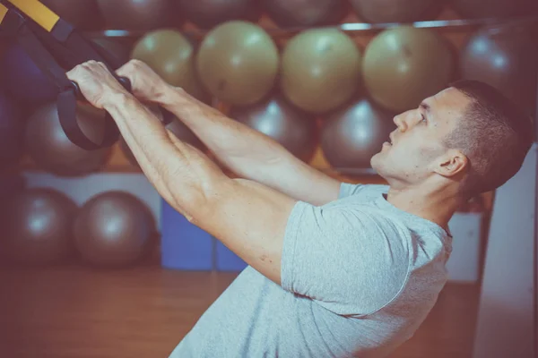 Young man is engaged in a gym in the trx — Stock Photo, Image