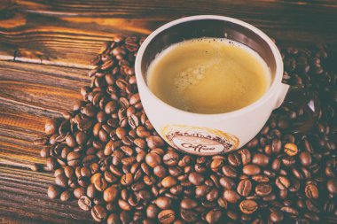 Tahta arka planda bir fincan kahve ve kahve çekirdeği.