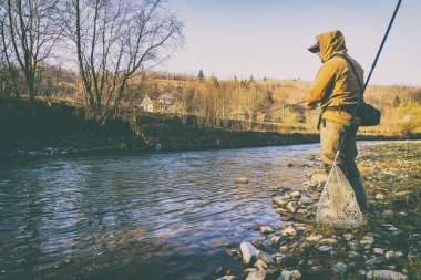 Balıkçı bir alabalık bir dağ nehir üzerinde yakalar.