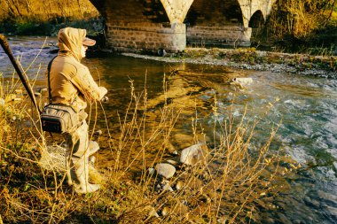 Balıkçı bir alabalık bir dağ nehir üzerinde yakalar.