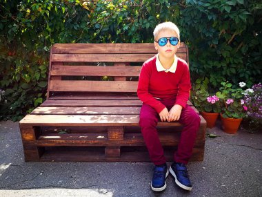 şık çocuk ahşap bir bankta oturur