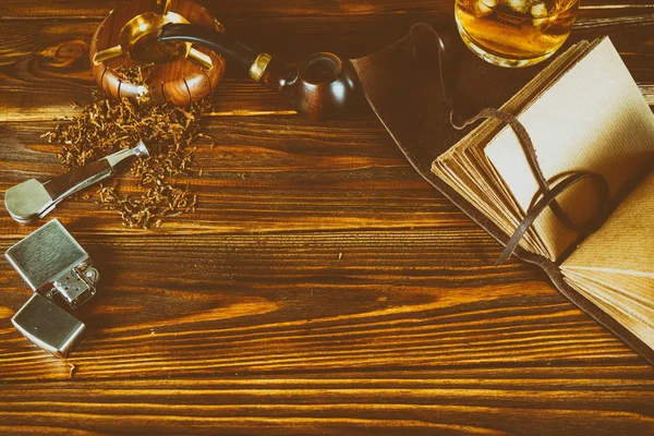 Sobre una mesa marrón una pipa humeante, tabaco, un encendedor, un whisky , — Foto de Stock