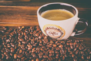 Tahta arka planda bir fincan kahve ve kahve çekirdeği.