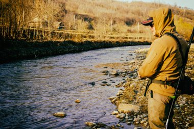 Balıkçı bir alabalık bir dağ nehir üzerinde yakalar.