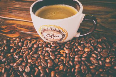 Tahta arka planda bir fincan kahve ve kahve çekirdeği.