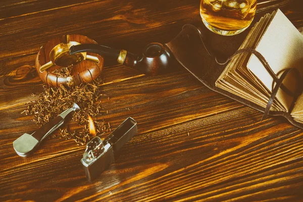 On a brown table a smoking pipe, tobacco, a lighter, a whiskey, — Stock Photo, Image