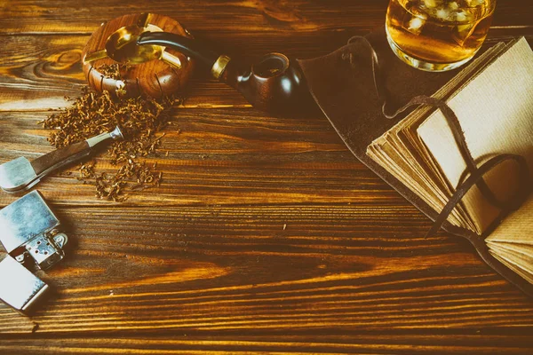 Sobre una mesa marrón una pipa humeante, tabaco, un encendedor, un whisky , — Foto de Stock