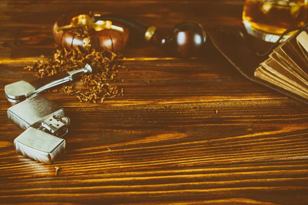 Na hnědém stole dýmka, tabák, zapalovač, whisky, — Stock fotografie