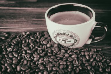 Tahta arka planda bir fincan kahve ve kahve çekirdeği.