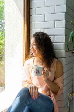 Pencerenin yanında kupası olan güzel bir kız.