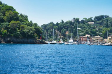 Harbor view of Portofino with sailing boats, yachts and the church of St. George on the hill in the background, Liguria, Italy.