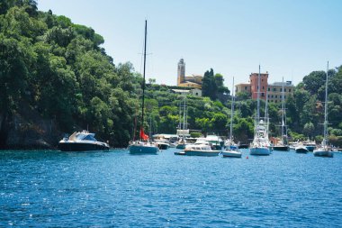 Harbor view of Portofino with sailing boats, yachts and the church of St. George on the hill in the background, Liguria, Italy.