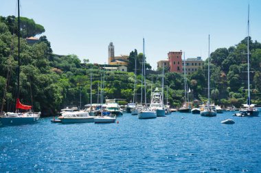 Harbor view of Portofino with sailing boats, yachts and the church of St. George on the hill in the background, Liguria, Italy.