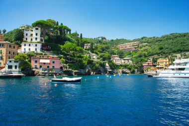 Harbor view of Portofino with sailing boats, yachts and the church of St. George on the hill in the background, Liguria, Italy.