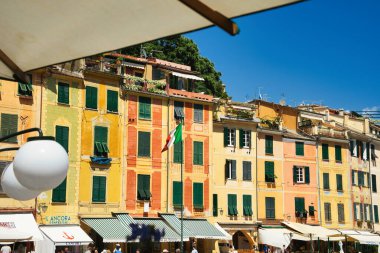 Renkli yüzlü, yeşil panjurlu ve açık mavi gökyüzünün altında çiçek açan çiçeklerle süslenmiş büyüleyici İtalyan evi..