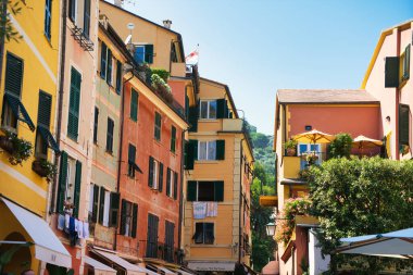Colorful narrow street in an Italian coastal town with traditional houses, balconies, and outdoor terraces on a sunny summer day.