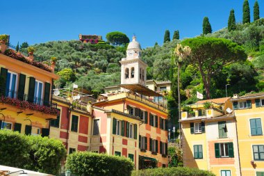 Colorful narrow street in an Italian coastal town with traditional houses, balconies, and outdoor terraces on a sunny summer day.
