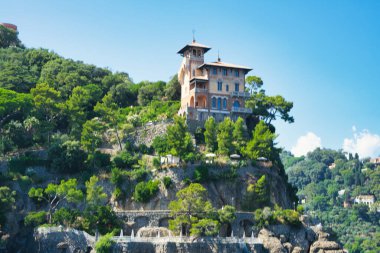 A villa standing on top of a cliff in Portofino, Italy, surrounded by greenery and terraces overlooking the sea.
