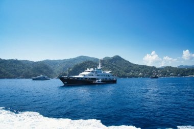 A speedboat glides across the blue waters of the Ligurian Sea with hills and coastline in the background.