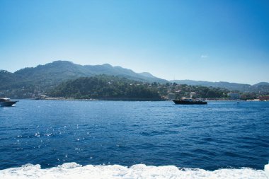 A speedboat glides across the blue waters of the Ligurian Sea with hills and coastline in the background.