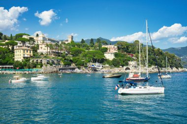 Scenic view of colorful buildings and yachts by the coast with green hills in the background in Liguria, Italy.