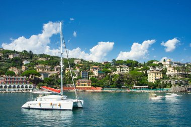 Scenic view of colorful buildings and yachts by the coast with green hills in the background in Liguria, Italy.