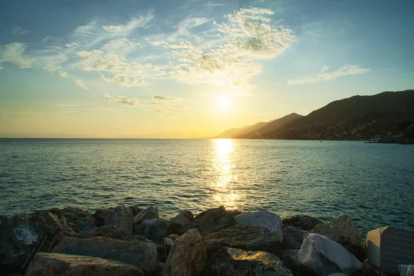 Sakin denizin üzerinde altın gün batımı, ufukta kayalık kıyı ve dağlar..