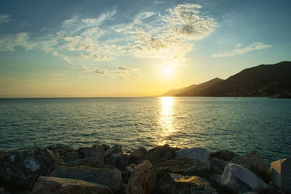 Sakin denizin üzerinde altın gün batımı, ufukta kayalık kıyı ve dağlar..