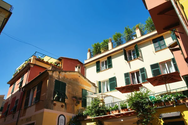 Renkli yüzlü, yeşil panjurlu ve açık mavi gökyüzünün altında çiçek açan çiçeklerle süslenmiş büyüleyici İtalyan evi..