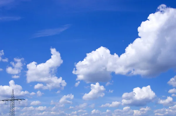 Flauschige Weisse Wolken Vor Blauem Himmel Ueber Strommast — Stock fotografie